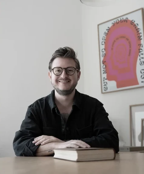 Vincent Templin, Art Director und Human Design Mentor des Holistic Playground, am Tisch mit einem Buch