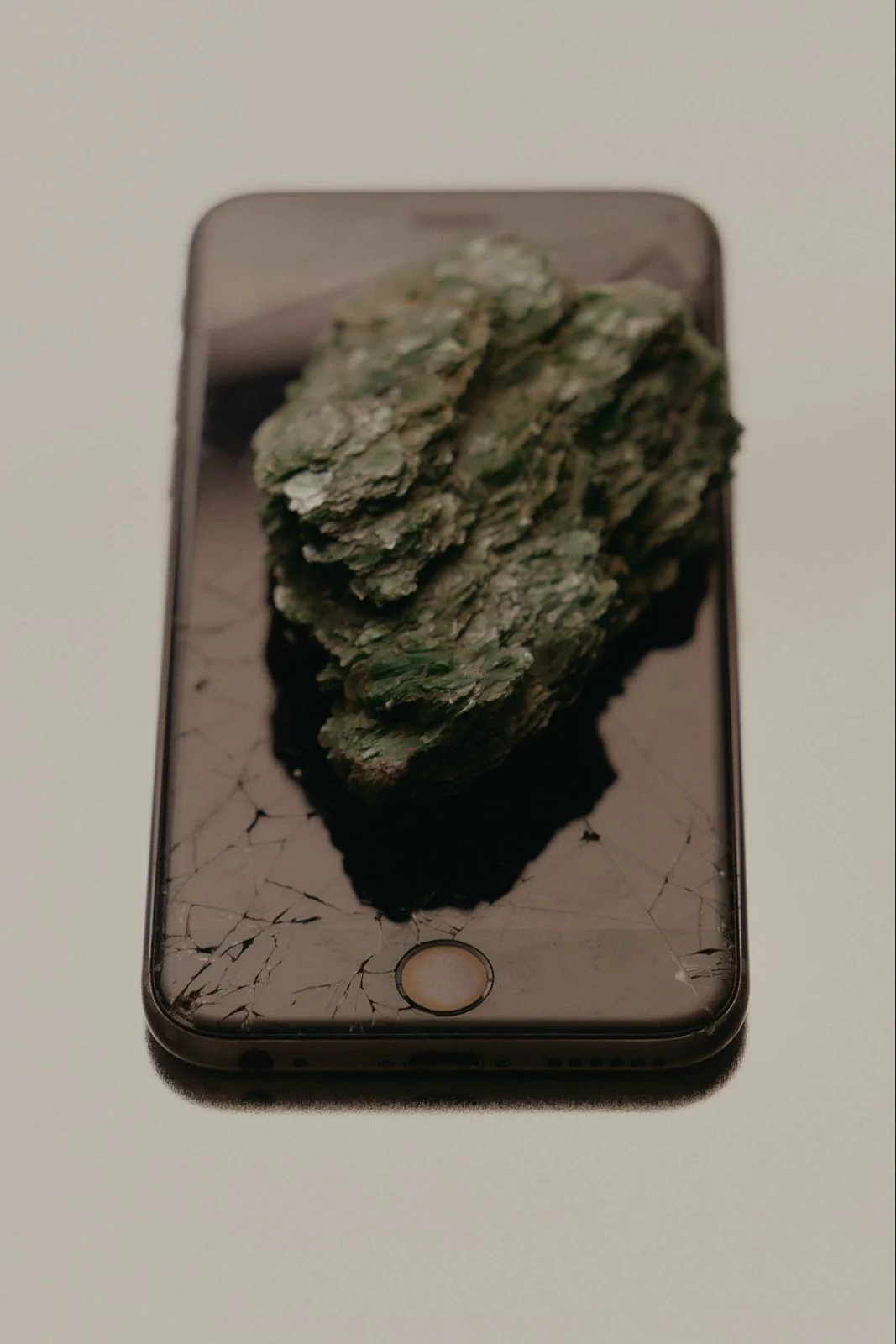 Ein moosbewachsener Stein liegt auf einem Smartphone mit gesprungenem Display, Sinnbild für digitale Pause