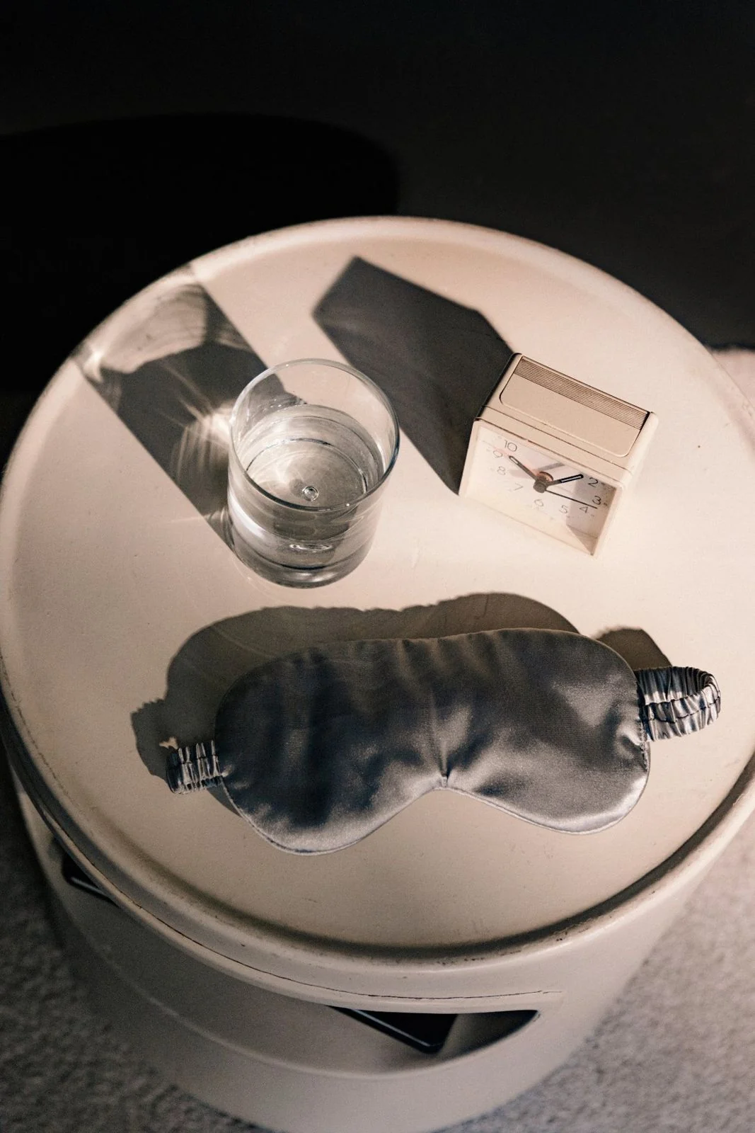 Stillleben mit Schlafmaske, Wasserglas und kleiner Schachtel auf einem runden Tisch, Sinnbild für Ruhe