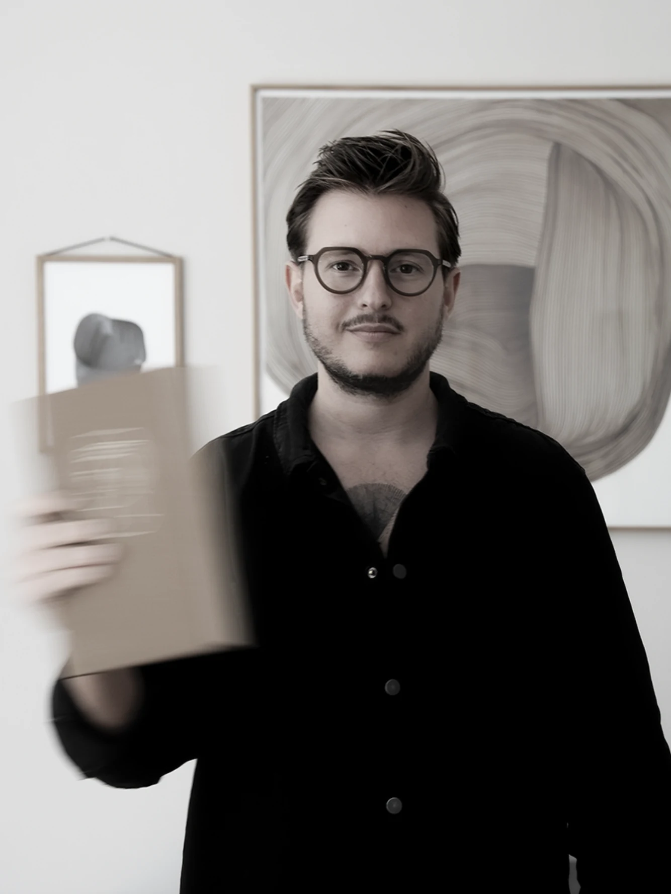 Vincent Templin, Art Director und Human Design Mentor des Holistic Playground, hält vor gerahmten Kunstdrucken ein Notizbuch in die Kamera