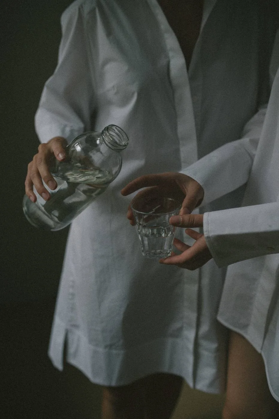 H\u00e4nde, die Wasser aus einer Glasflasche in ein Glas gie\u00dfen
